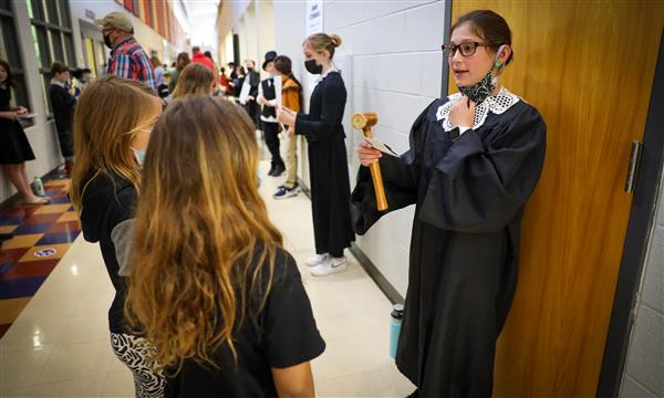 A girl dressed as Ruth Bader Ginsberg speaks to younger students
